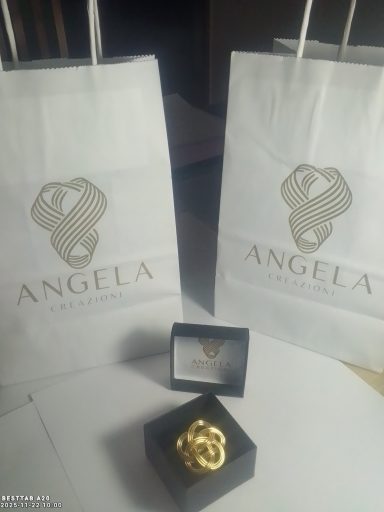 Two white gift bags with "ANGELA" printed on them, and a gold jewelry piece in a box.